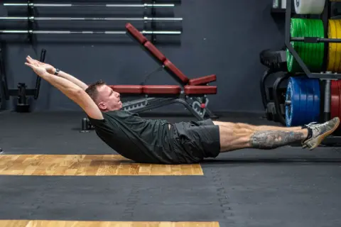 Mężczyzna wykonuje ćwiczenie hollow body hold na siłowni, napinając mięśnie brzucha.