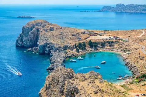 Malownicza zatoka na Rodos, idealna do zwiedzania samochodem. Woda krystalicznie czysta, plaża pełna ludzi, a wokół skaliste wybrzeże.