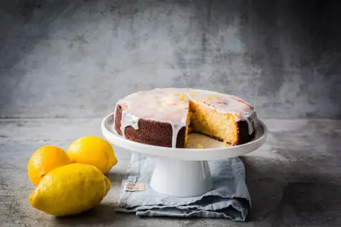 Ein saftiger zitronenkuchen mit Zuckerguss und Zitronenschale, daneben frische Zitronen.