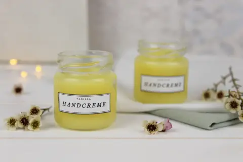 Zwei Gläser mit selbstgemachter Handcreme, verziert mit kleinen Blüten. Perfekt zum Handcreme selber machen für Kinder.