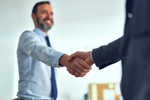 Uśmiechnięty mężczyzna w koszuli i krawacie ściska dłoń partnerowi biznesowemu. Pozytywne axpo polska opinie potwierdzone gestem.