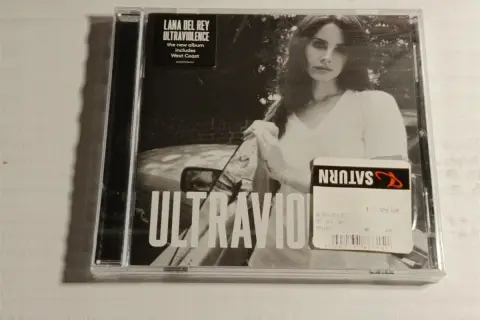 Okładka płyty Lana Del Rey Ultraviolence. Na czarno-białym zdjęciu artystka w białej koszulce, obok naklejka Saturn z ceną.
