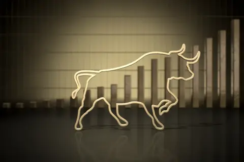 Złoty byk symbolizuje hossę, wzrosty na giełdzie. W tle wykres słupkowy pnący się w górę.