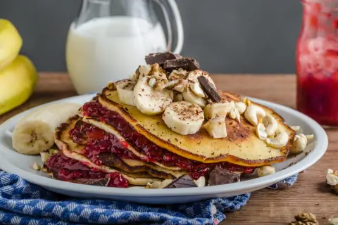 Stos puszystych, trzyskładnikowych placków bananowych z malinową konfiturą, bananami, orzechami i czekoladą.