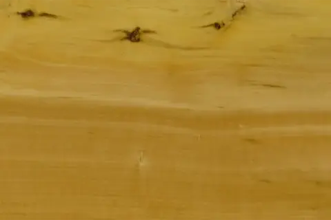 Textura de madera de boj con vetas doradas y nudos oscuros, evocando la calidez de un mueble antiguo.