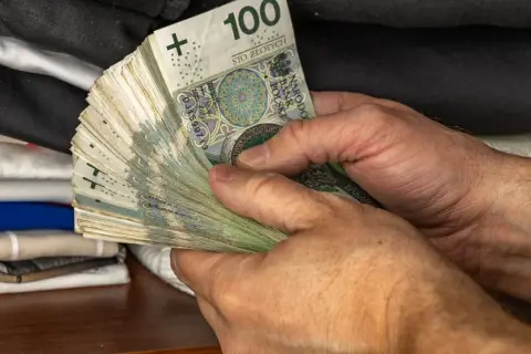 Dłonie trzymające plik banknotów 100 zł. To jeden z elementów, który wpływa na narzędzia polityki pieniężnej.