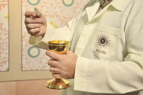 Dłoń trzymająca hostię i złoty kielich podczas ceremonii religijnej.