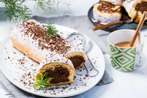 Rolada biszkoptowa z czekoladowym nadzieniem, posypana cukrem pudrem i wiórkami czekolady.