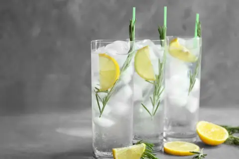 Trzy orzeźwiające gin fizz z lodem, plasterkami cytryny i gałązkami rozmarynu, ozdobione zielonymi słomkami.