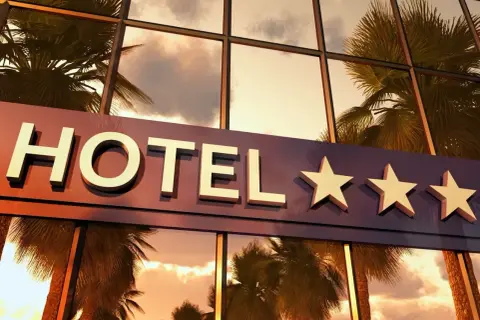 Napis "HOTEL" z trzema gwiazdkami na tle odbijających się palm i nieba.