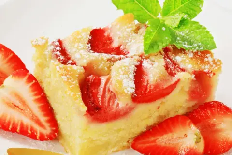 Ein saftiger Erdbeer Blechkuchen, bestäubt mit Puderzucker und garniert mit frischen Erdbeeren und Minze.