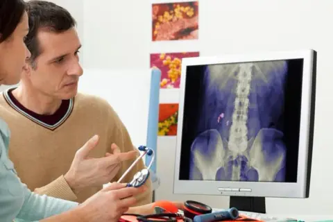 Medico e paziente esaminano una radiografia che mostra calcoli renali, possibile indicazione di malattia di Berger e potenziale invalidità.