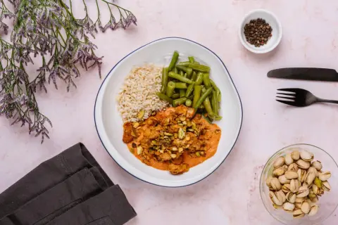 Talerz z ryżem, fasolką szparagową i kurczakiem w sosie z pistacjami. Obok naczynie z orzechami.