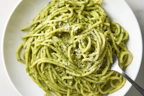 Pyszny makaron z pesto, posypany parmezanem, czeka na widelcu. Idealny na szybki obiad.