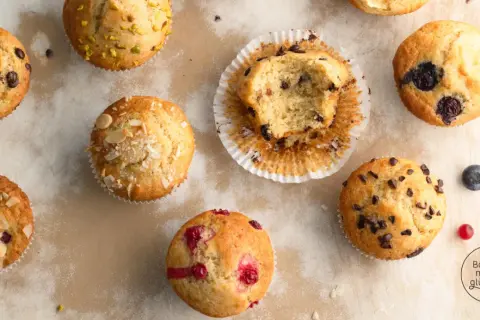 Verschiedene Muffins, die nach einem Muffins Grundrezept gebacken wurden: mit Schokostückchen, Blaubeeren, Himbeeren und Mandeln. Einer ist angeknabbert.