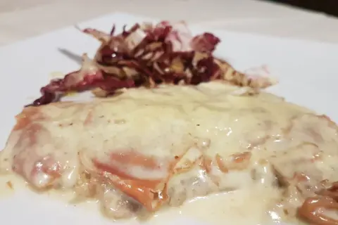Deliziosa cotoletta alla bolognese, dorata e ricoperta da una cremosa salsa, accompagnata da radicchio croccante.