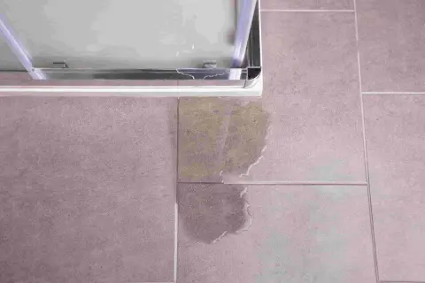Une fuite sous le bac à douche, une situation qui peut nécessiter une intervention d'assurance. L'eau s'est répandue sur le carrelage.