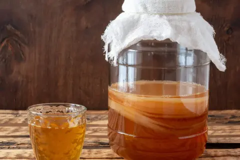Szklanka z napojem i duży słój z warstwową kulturą SCOBY – tak wygląda domowa kombucha.