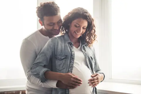 Un couple heureux, le futur papa enlace tendrement le ventre arrondi de sa compagne. Ils pensent déjà au prénom en N pour leur bébé.