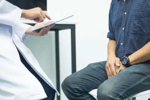 Lekarz pokazuje pacjentowi wyniki badań na tablecie. Czy biopsja oznacza raka? Pacjent z niepokojem czeka na diagnozę.