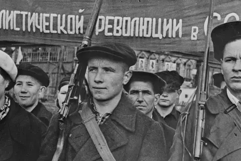 Ungdomar marscherar med en fana som nämner "socialistiska revolutionen". En del bär vapen. En tidslinje för ryska revolutionen kan illustreras av sådana scener.