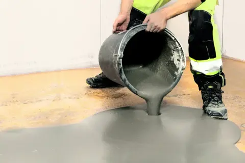 Arbetare häller jordfuktad betong från en hink för att jämna ut ett golv.