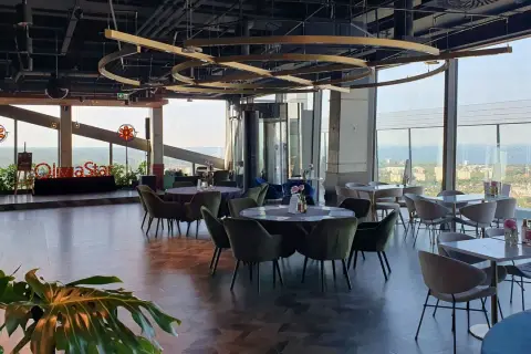 Eleganckie wnętrze restauracji Olivia Star z widokiem na miasto i morze. Stoły nakryte, gotowe na przyjęcie gości.