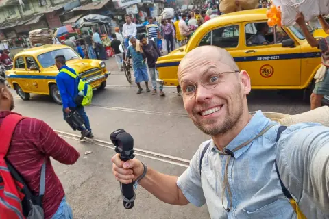 Uśmiechnięty turysta w okularach na tle żółtej taksówki i gwarnego ulicznego życia. To są jego wymarzone indie wczasy!