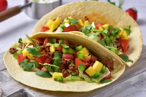 Dwa tacos z mielonym mięsem, pomidorami, papryką, mango i kolendrą na desce.