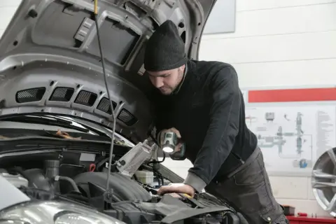 Mechanik z latarką bada silnik Renault, szukając przyczyny błędu DTC P0380.