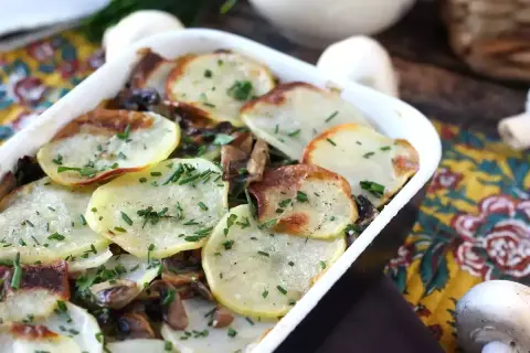 Zapiekanka ziemniaczana z pieczarkami, posypana szczypiorkiem, w białym naczyniu.