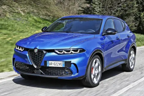 Niebieski SUV marki Alfa Romeo pędzi po asfaltowej drodze, otoczony zielenią.