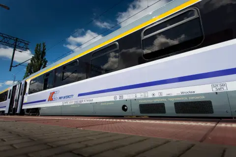 Pociąg Heweliusz PKP Intercity z Wrocławia, z widocznymi zbiornikami powietrza i klimatyzacją, na tle błękitnego nieba z chmurami.