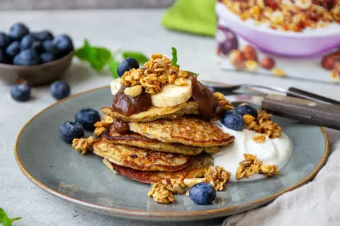 En hög med bananpannkakor toppas med banan, sylt och granola. Ett perfekt bananpannkaka recept för en lyxig frukost eller brunch.