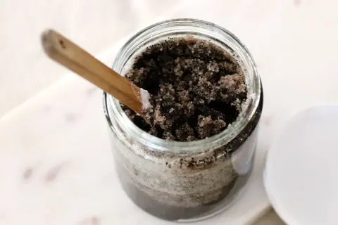 Słoik z domowym peelingiem z kawy, gotowy do użycia. Drewniana łyżeczka zanurzona w bogatej mieszance.