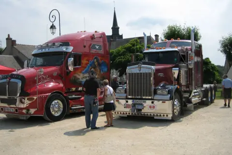 Deux camions américains tuning, l'un rouge vif avec une peinture personnalisée, l'autre bordeaux, se dressent fièrement.