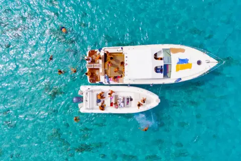 Gente si gode il mare di Favignana, nuotando e rilassandosi su due barche in acque cristalline.