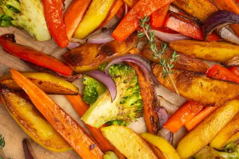 Un assortiment coloré de légumes rotis au four : carottes, pommes de terre, brocolis et oignons rouges, parsemés de thym frais.