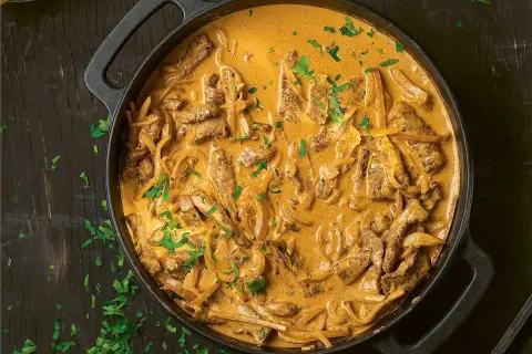 En krämig biff stroganoff i en gjutjärnspanna, toppad med färsk persilja.