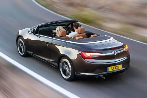 Para podróżuje lśniącym, ciemnobrązowym **Opel cabrio** po krętej drodze.