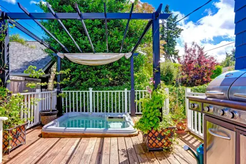 Un coin jacuzzi extérieur sous une pergola, avec un barbecue à proximité, invite à la détente.