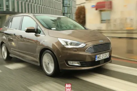 Brązowy Ford Grand C-Max w ruchu miejskim, z widocznymi kroplami deszczu na karoserii i rozmazanym tłem.