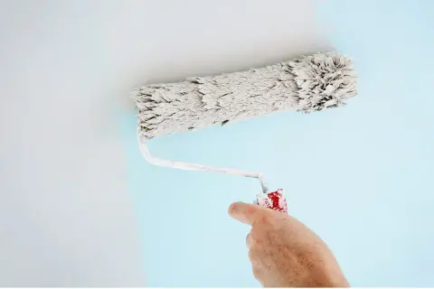 Main d'un peintre utilisant un rouleau pour appliquer une peinture bleu pâle sur un mur. Quel rouleau pour peinture velours !