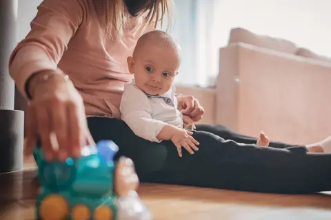 Mama bawi się z 9-miesięcznym dzieckiem, które siedzi na jej kolanach. Przed nimi leży zabawkowy pociąg.
