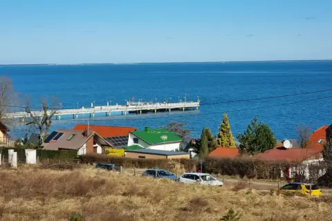 Widok na morze i molo w Mechelinkach. Domy z czerwonymi i zielonymi dachami, samochody na drodze. Mechelinki atrakcje to spacer po molo i podziwianie krajobrazu.