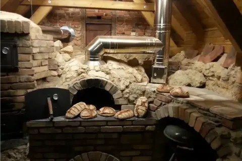 Frisches Brot wird im Pizzaofen gebacken. Mehrere Laibe liegen bereit, einige sind schon im Ofen.