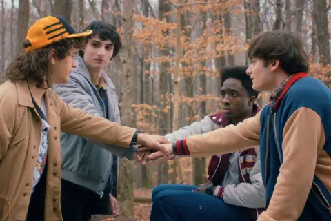 Czterech przyjaciół z Stranger Things w lesie, łączących dłonie.