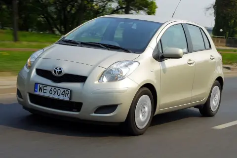 Złoty Toyota Yaris 2006 na drodze, z zielenią w tle.