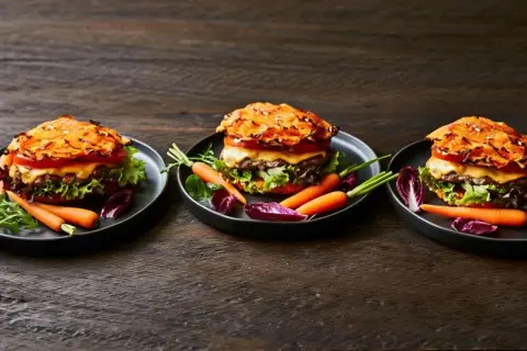 Drei appetitliche Hamburger mit Pommes, garniert mit Karotten und Radicchio auf dunklem Holztisch.