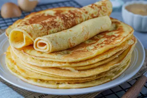 Ein Stapel goldbrauner Eierkuchen, zwei davon gerollt, warten auf ein leckeres Eierkuchen Rezept.